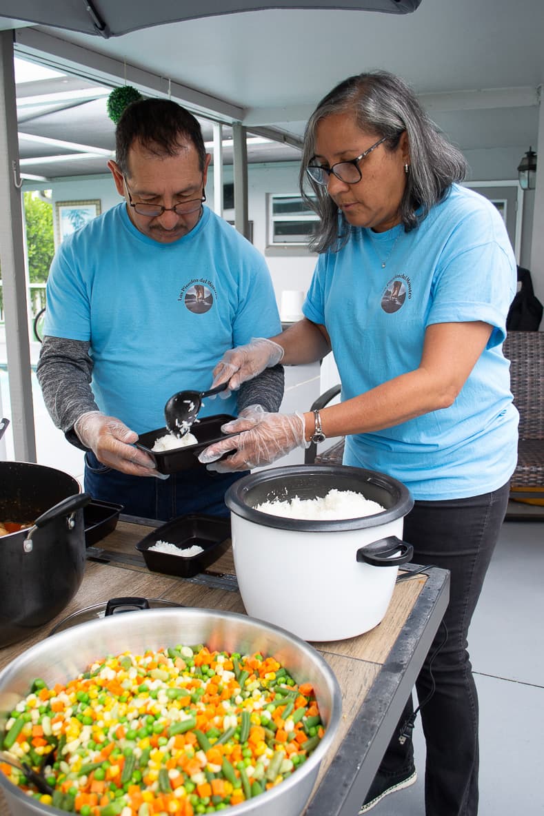 Volunteers serving rice and vegetables onto trays for delivery
